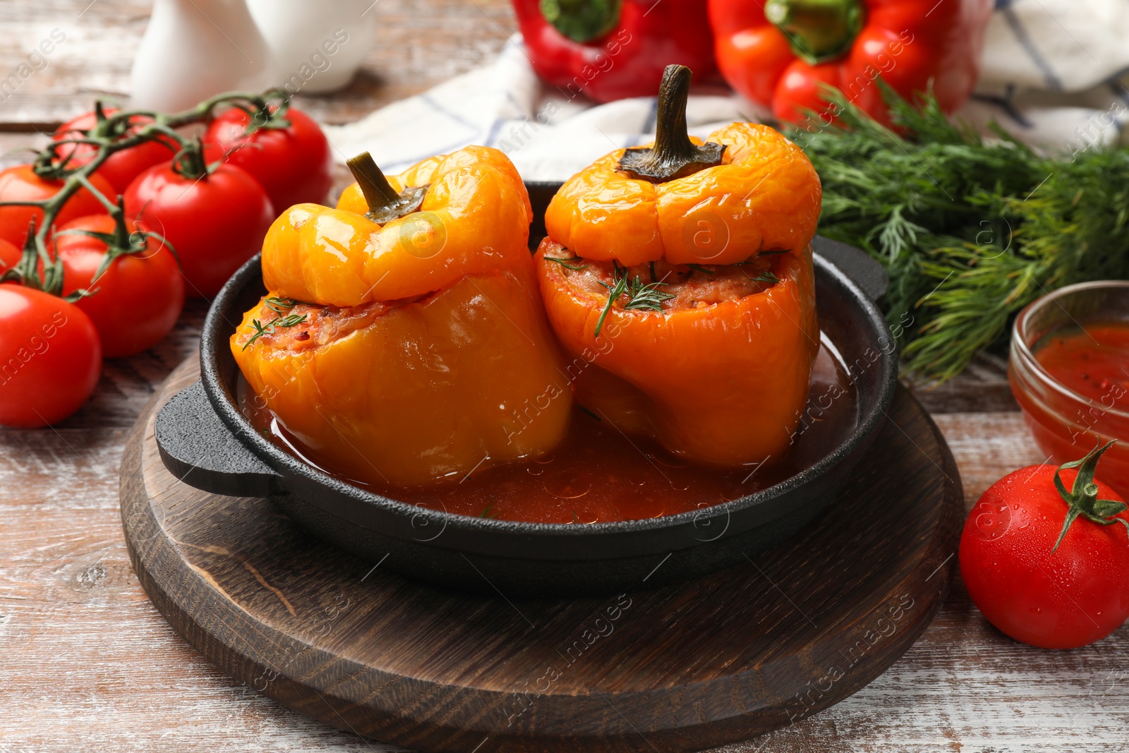 Photo of Tasty stuffed peppers in pan and products on wooden rustic table, closeup