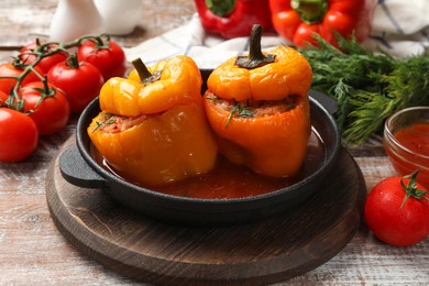 Photo of Tasty stuffed peppers in pan and products on wooden rustic table, closeup