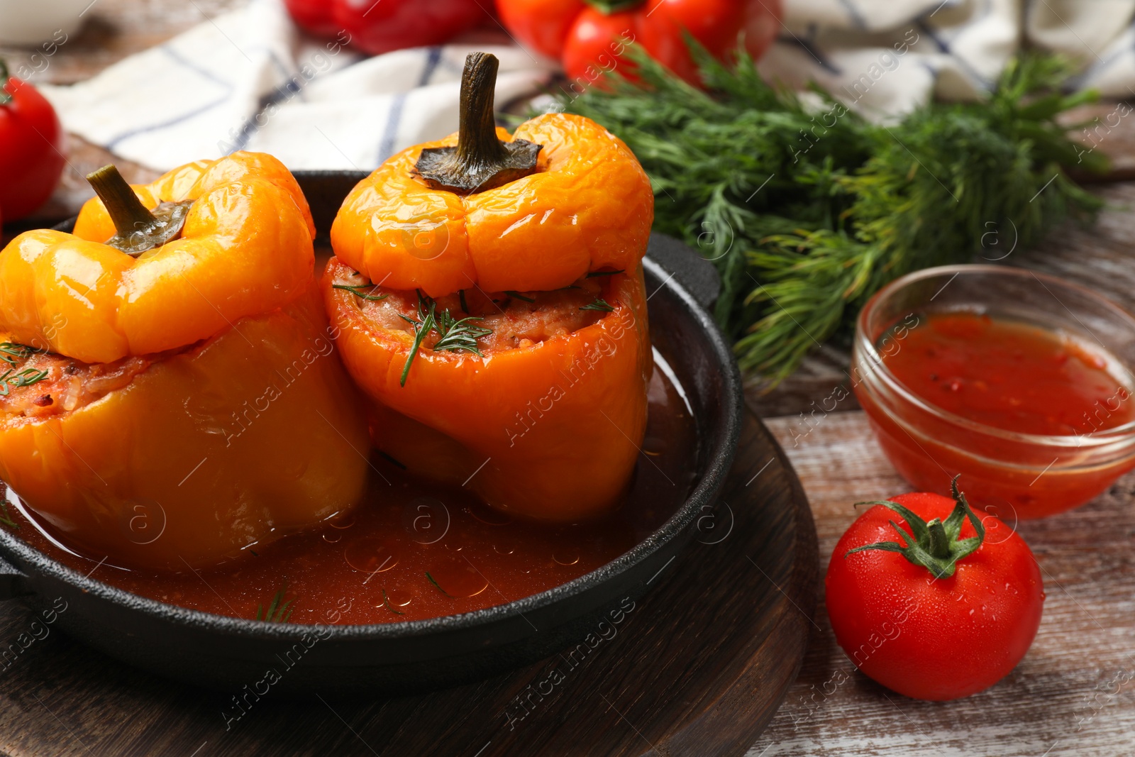 Photo of Tasty stuffed peppers in pan, sauce and tomato on wooden rustic table, closeup