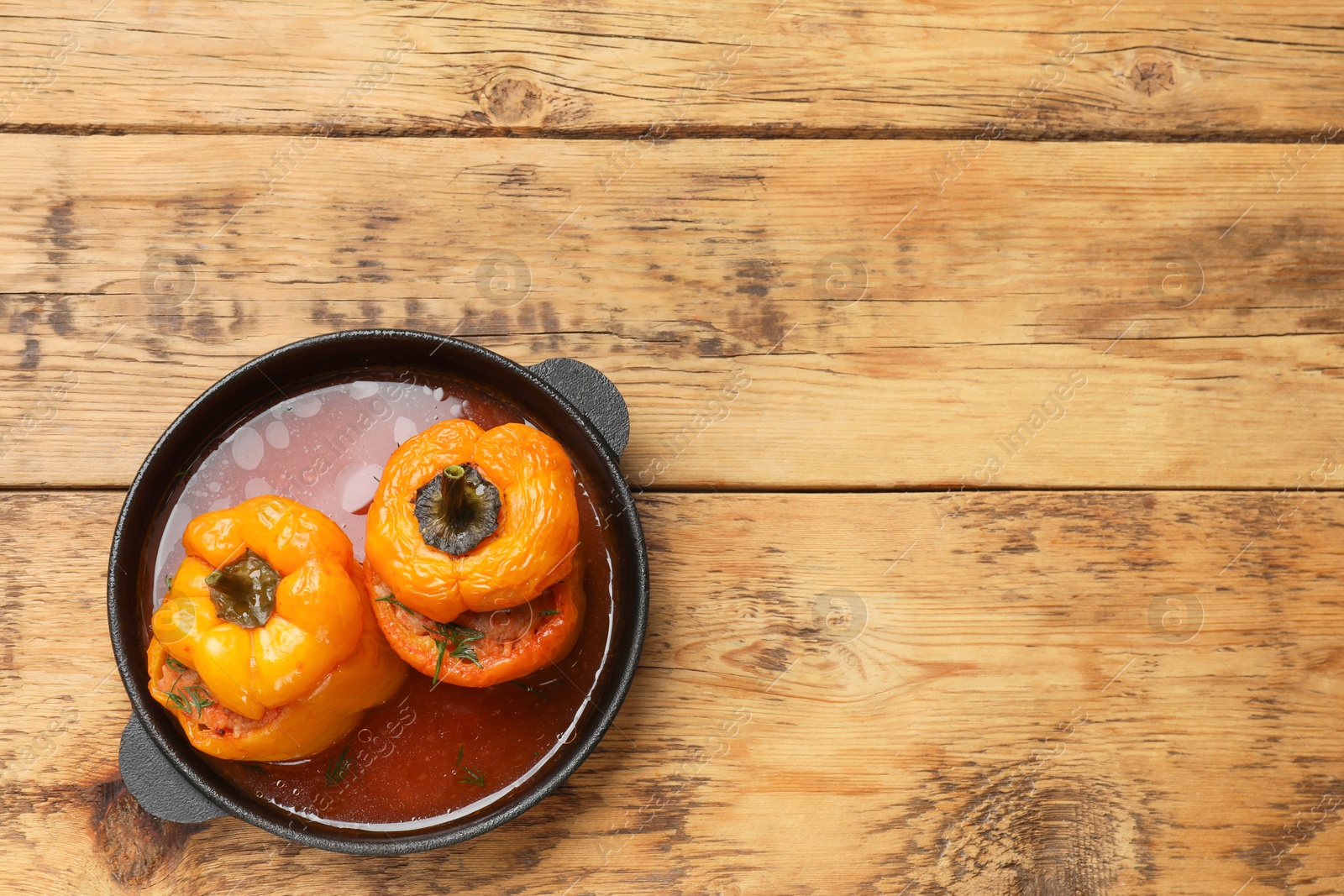 Photo of Tasty stuffed peppers in pan on wooden table, top view. Space for text