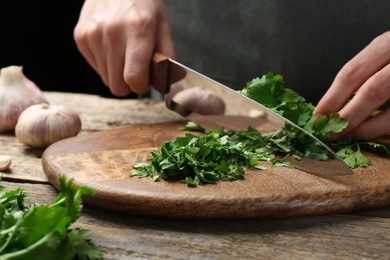 Photo of Woman cutting fresh coriander at wooden table, closeup