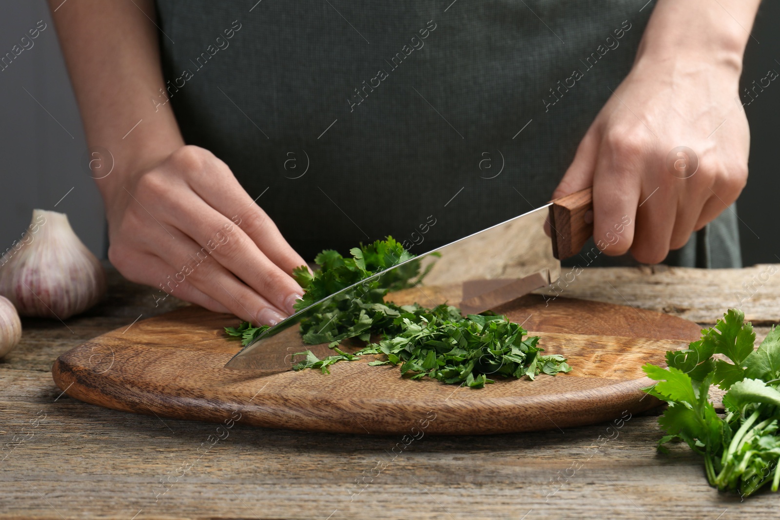 Photo of Woman cutting fresh coriander at wooden table, closeup