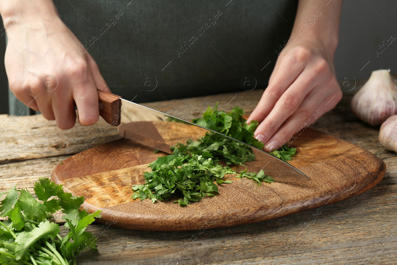 Photo of Woman cutting fresh coriander at wooden table, closeup