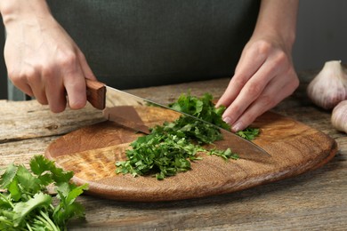 Woman cutting fresh coriander at wooden table, closeup