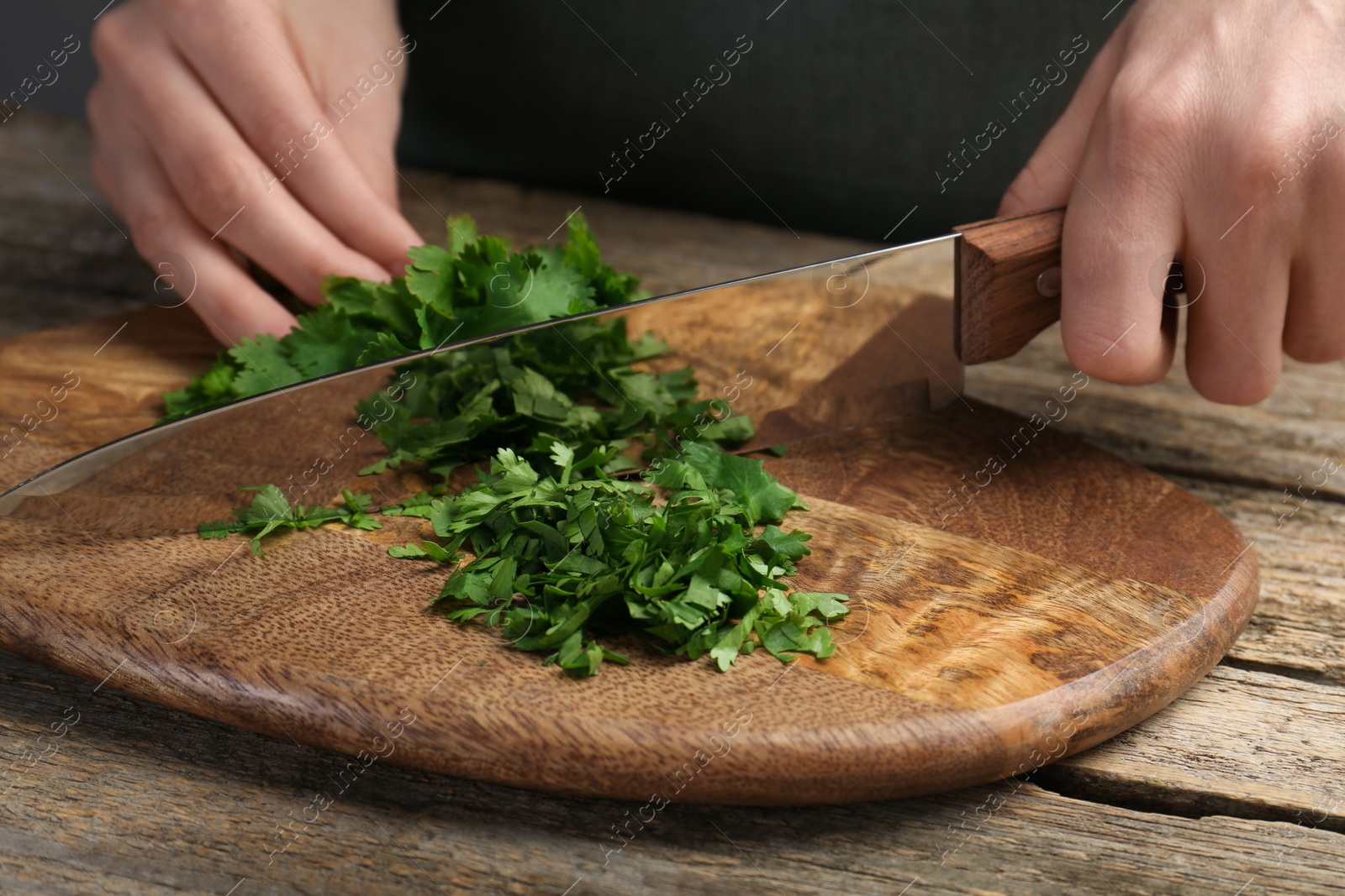 Photo of Woman cutting fresh coriander at wooden table, closeup