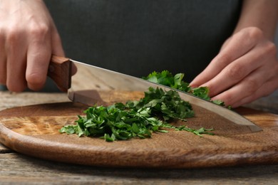 Woman cutting fresh coriander at wooden table, closeup