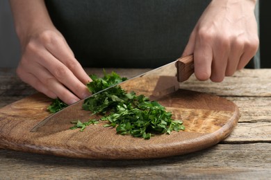 Photo of Woman cutting fresh coriander at wooden table, closeup