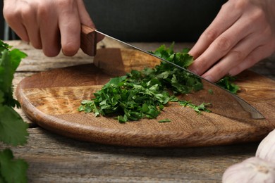 Woman cutting fresh coriander at wooden table, closeup