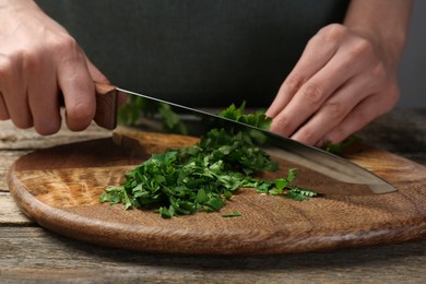 Photo of Woman cutting fresh coriander at wooden table, closeup