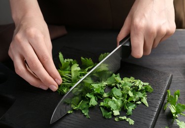 Photo of Woman cutting fresh coriander at black wooden table, closeup