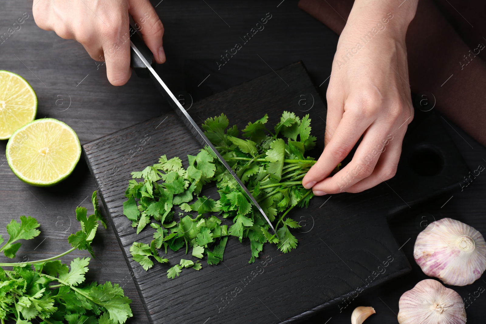 Photo of Woman cutting fresh coriander at black wooden table, closeup