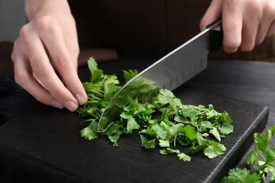 Woman cutting fresh coriander at black wooden table, closeup