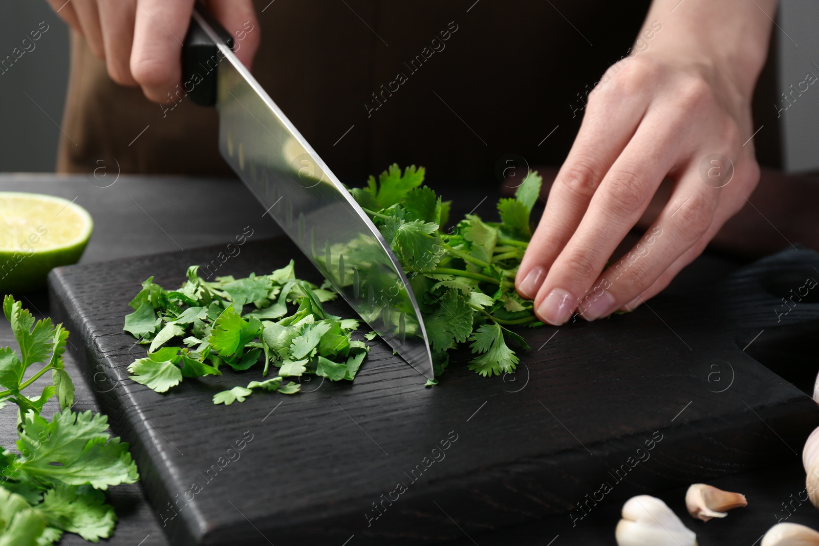 Photo of Woman cutting fresh coriander at black wooden table, closeup
