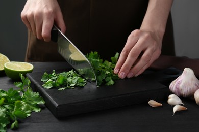 Photo of Woman cutting fresh coriander at black wooden table, closeup