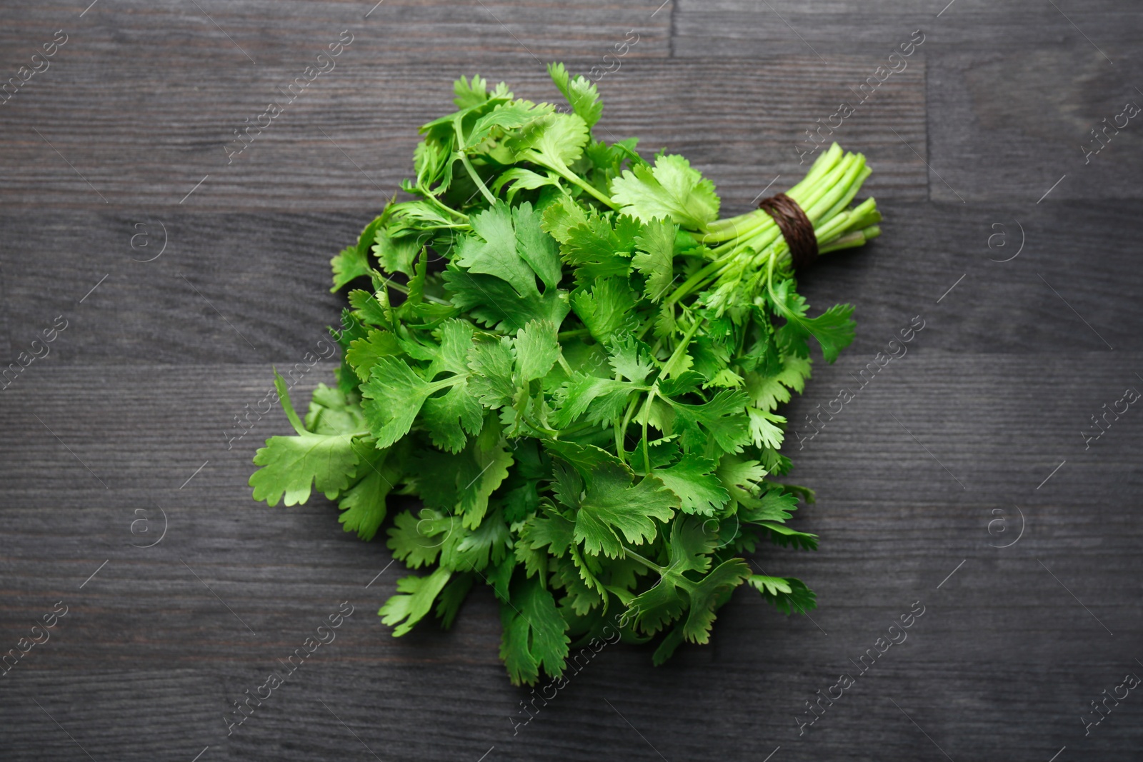 Photo of Bunch of fresh coriander on black wooden table, top view