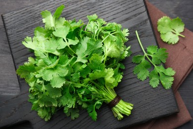 Photo of Bunch of fresh coriander on black wooden table, top view