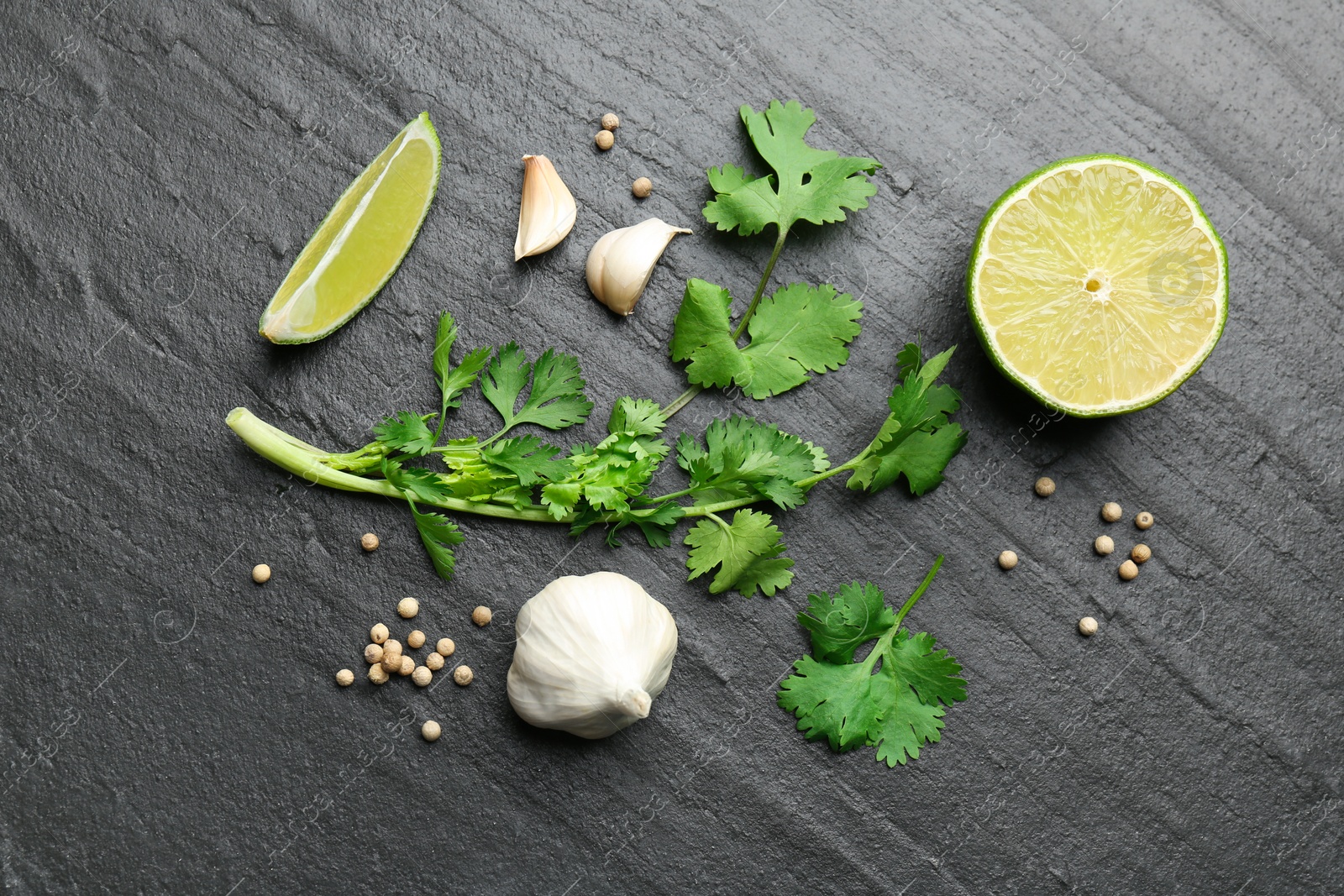 Photo of Fresh coriander leaves, dried seeds, garlic and lime on black textured table, flat lay