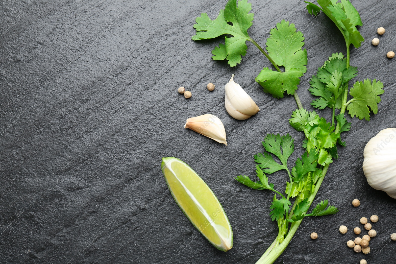 Photo of Fresh coriander leaves, dried seeds, garlic and lime on black textured table, flat lay. Space for text