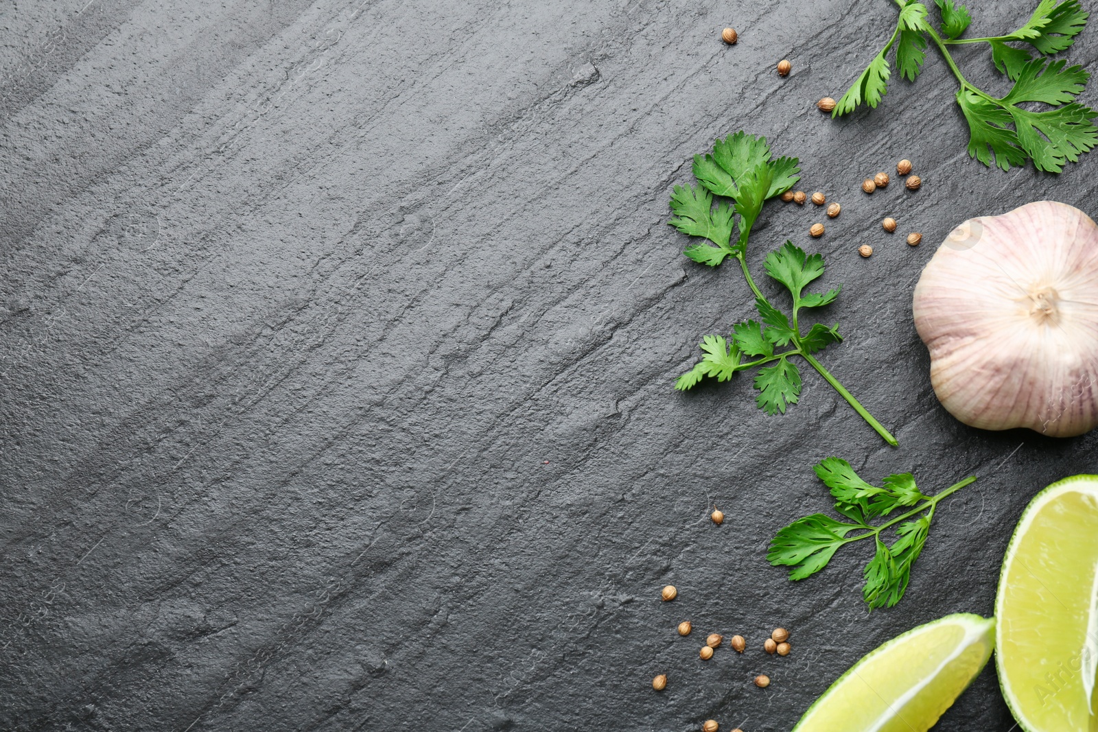 Photo of Fresh coriander leaves, dried seeds, garlic and lime wedges on black textured table, flat lay. Space for text