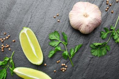 Fresh coriander leaves, dried seeds, garlic and lime wedges on black textured table, flat lay