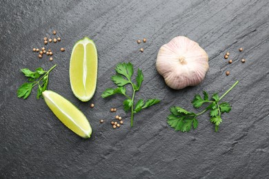 Fresh coriander leaves, dried seeds, garlic and lime wedges on black textured table, flat lay