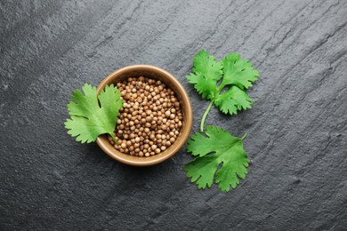 Photo of Fresh green coriander leaves and dried seeds on black table, flat lay