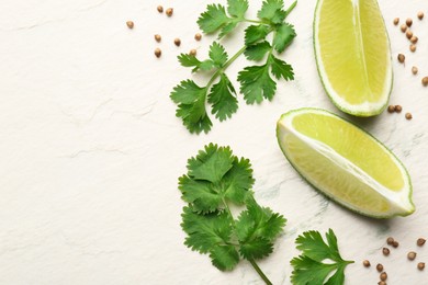 Fresh coriander leaves, dried seeds and lime wedges on light textured table, flat lay. Space for text