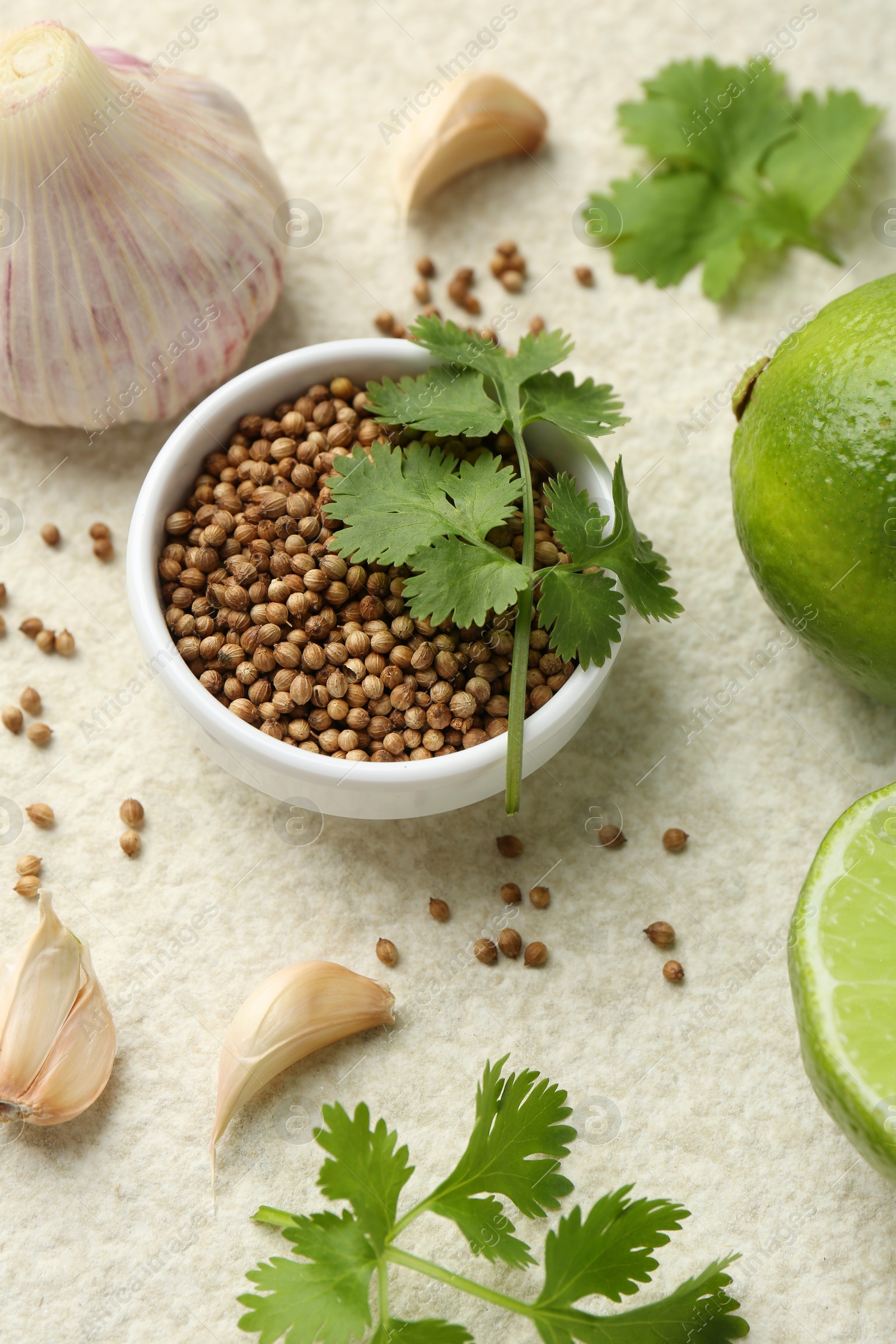 Photo of Fresh coriander leaves, dried seeds, garlic and limes on light textured table
