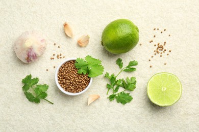 Fresh coriander leaves, dried seeds, garlic and limes on light textured table, flat lay
