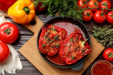 Photo of Tasty stuffed peppers in dish and ingredients on wooden table, flat lay