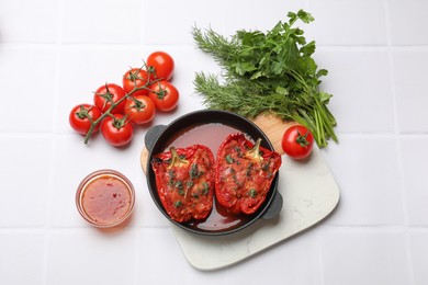 Photo of Tasty stuffed peppers in dish and ingredients on white tiled table, flat lay