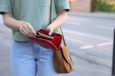 Woman holding purse with banknotes outdoors, closeup. Space for text