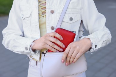 Photo of Woman putting purse into bag outdoors, closeup