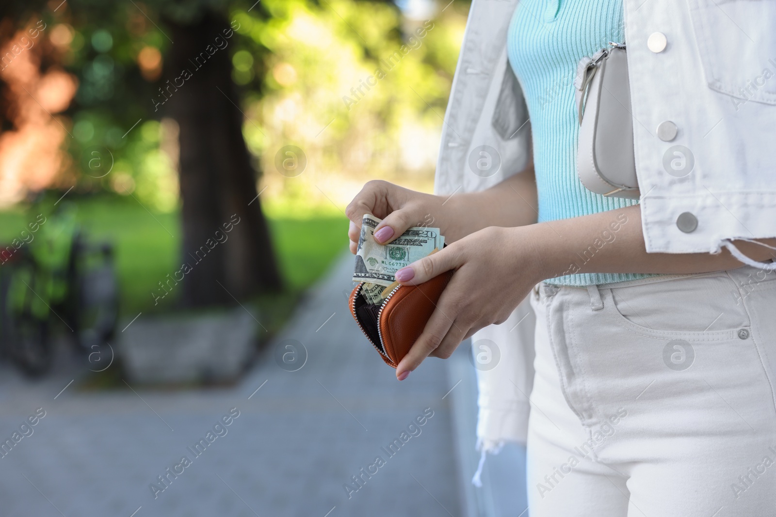 Photo of Woman holding purse with banknotes outdoors, closeup. Space for text