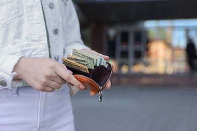 Woman holding purse with banknotes outdoors, closeup. Space for text