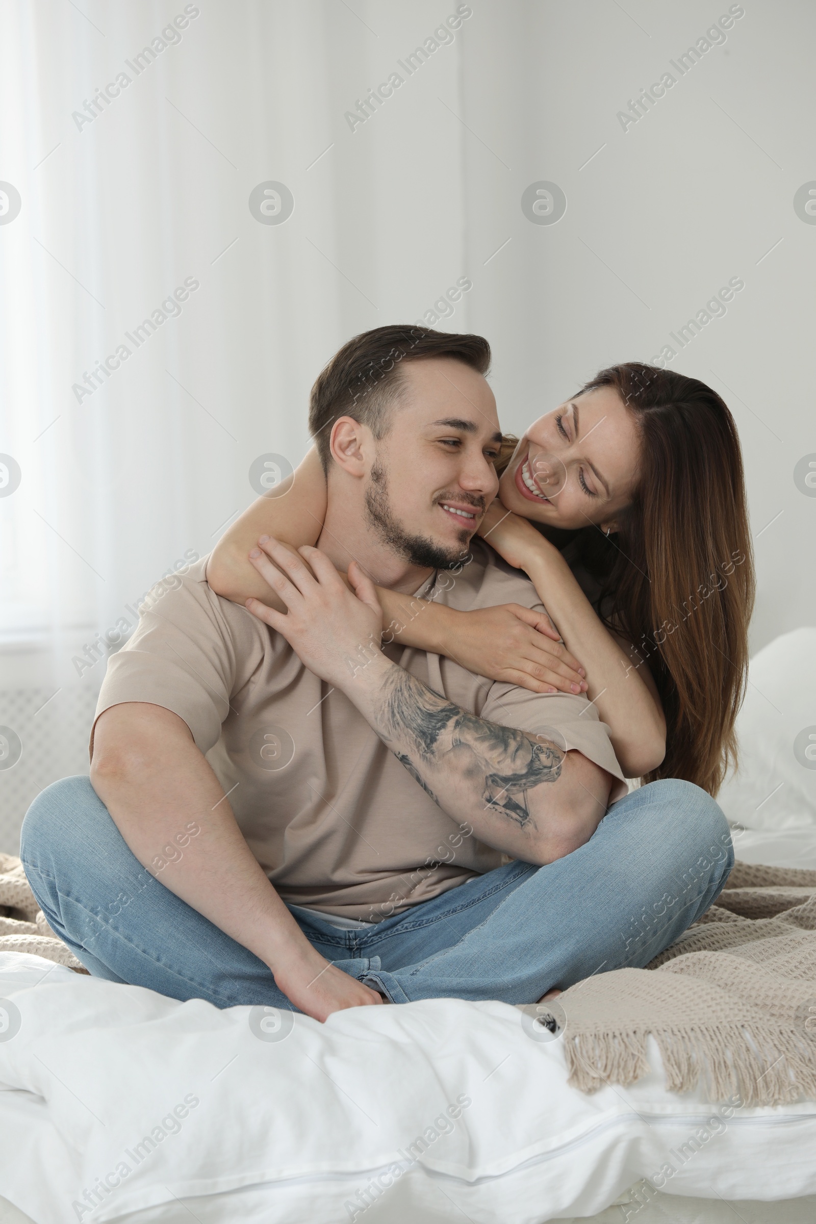 Photo of Happy couple sitting on bed and hugging at home