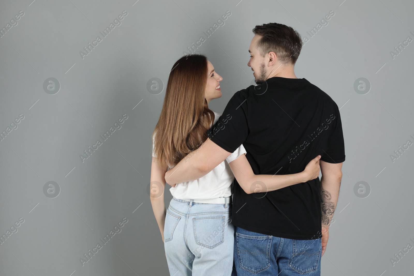 Photo of Cute couple hugging on grey background, back view. Space for text