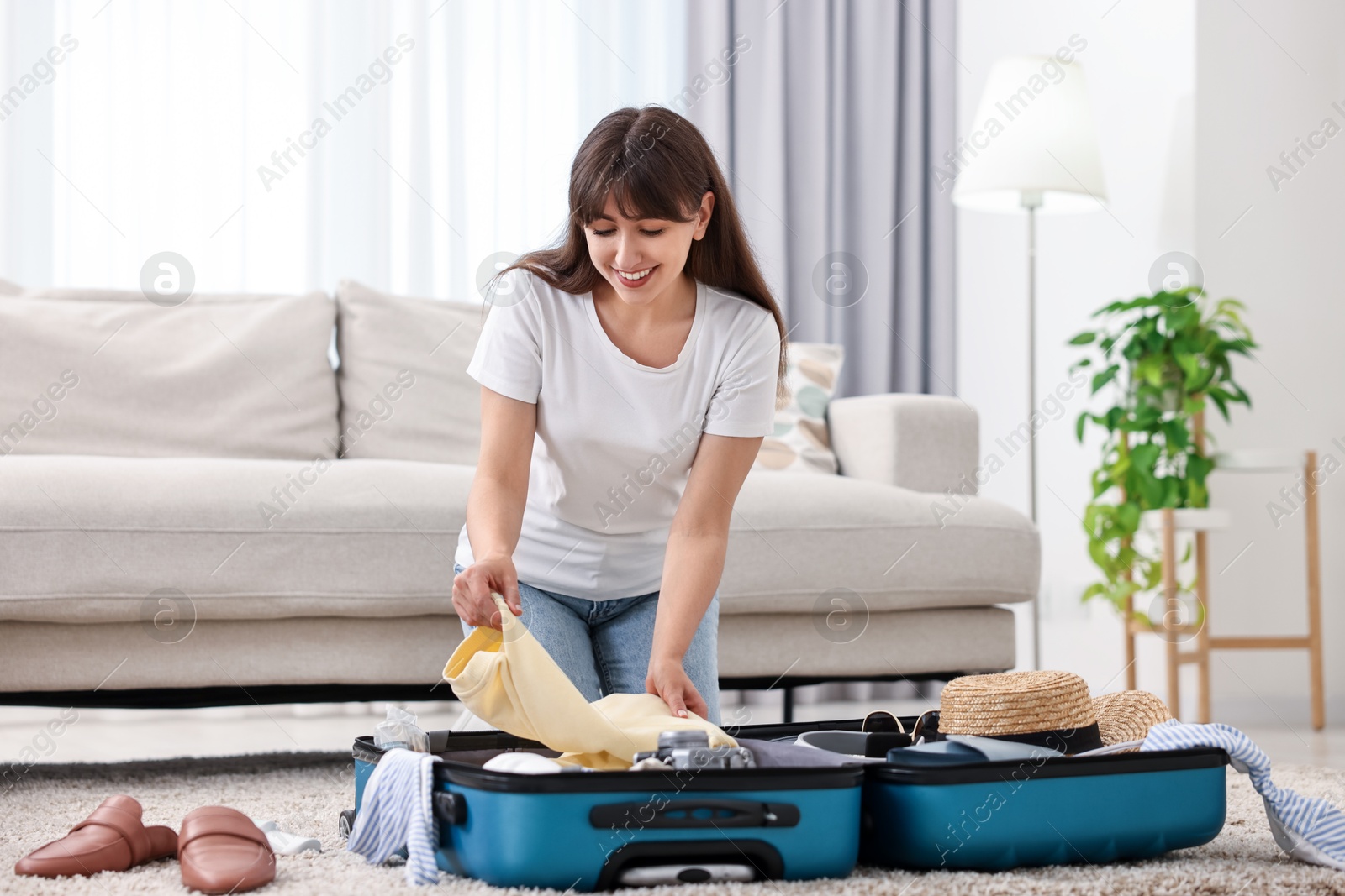 Photo of Woman packing suitcase for trip on floor indoors