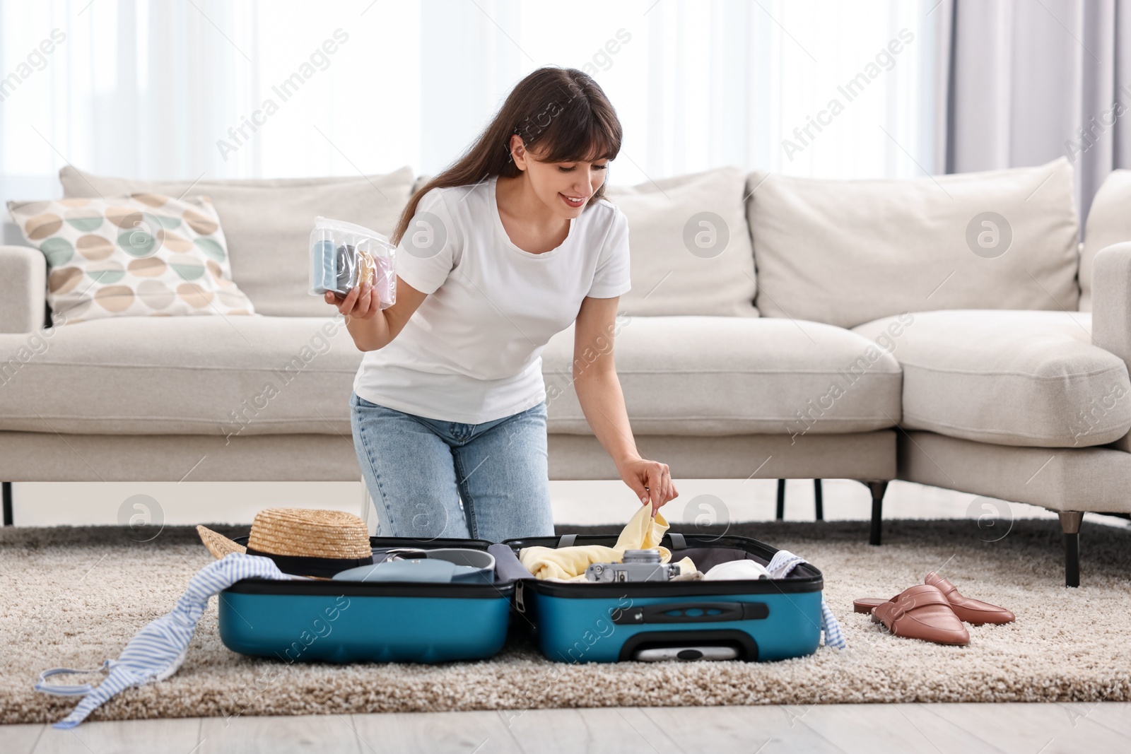 Photo of Woman packing suitcase for trip on floor indoors