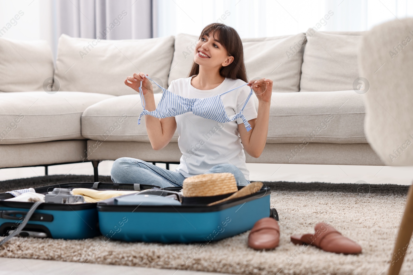 Photo of Woman packing suitcase for trip on floor indoors