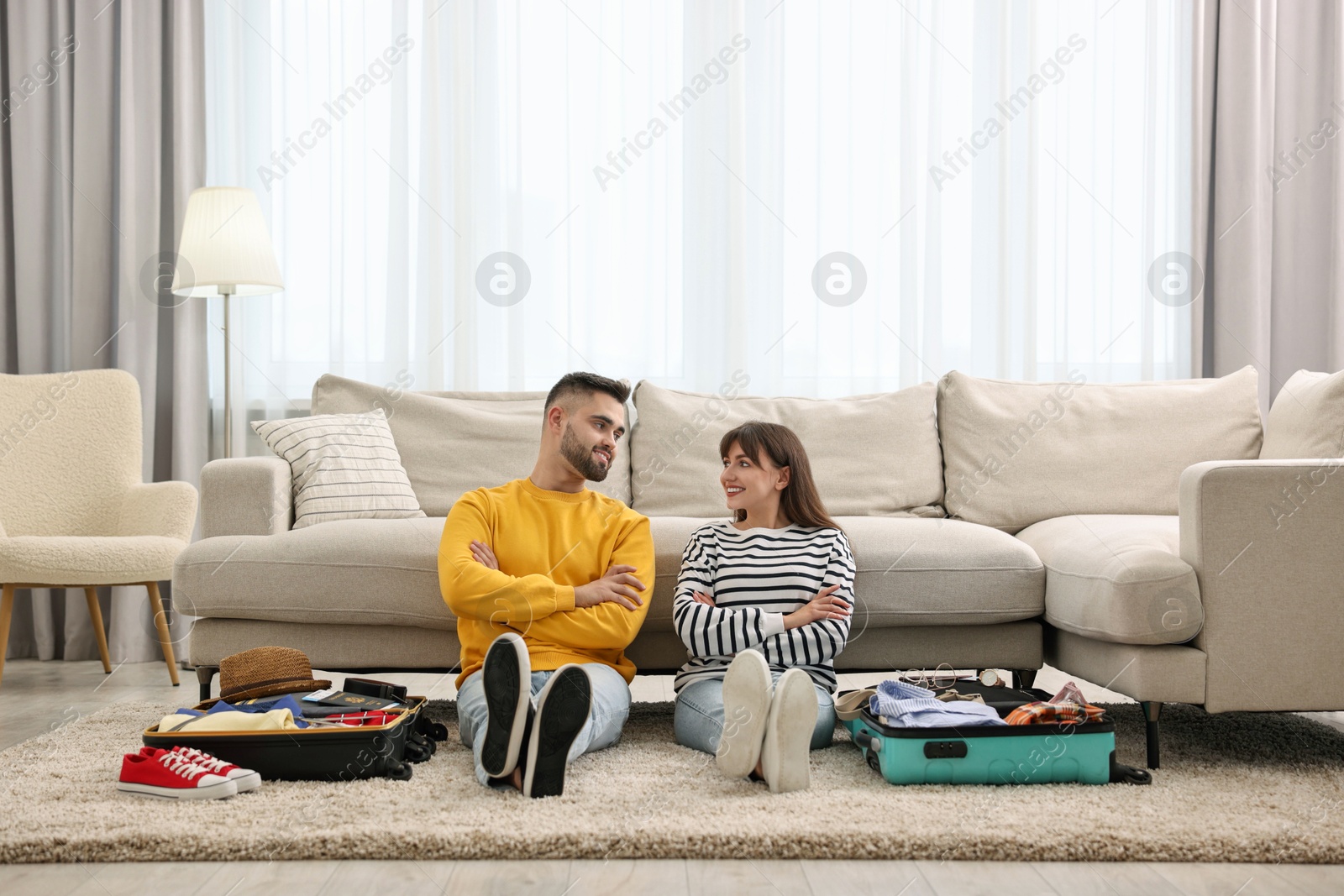 Photo of Couple near suitcases with clothes on floor indoors