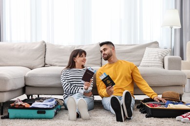 Couple with passports and tickets near suitcases on floor indoors