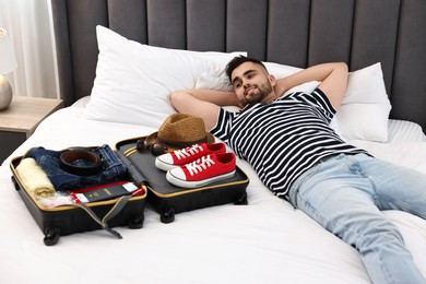Man near suitcase with clothes on bed indoors