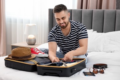 Photo of Man packing suitcase for trip on bed indoors