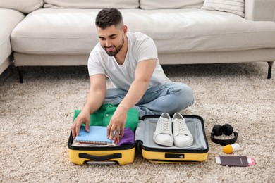 Photo of Man packing suitcase on floor at home