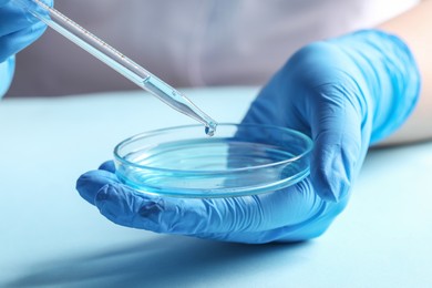 Photo of Doctor dripping liquid from pipette into petri dish at light table, closeup. Laboratory analysis