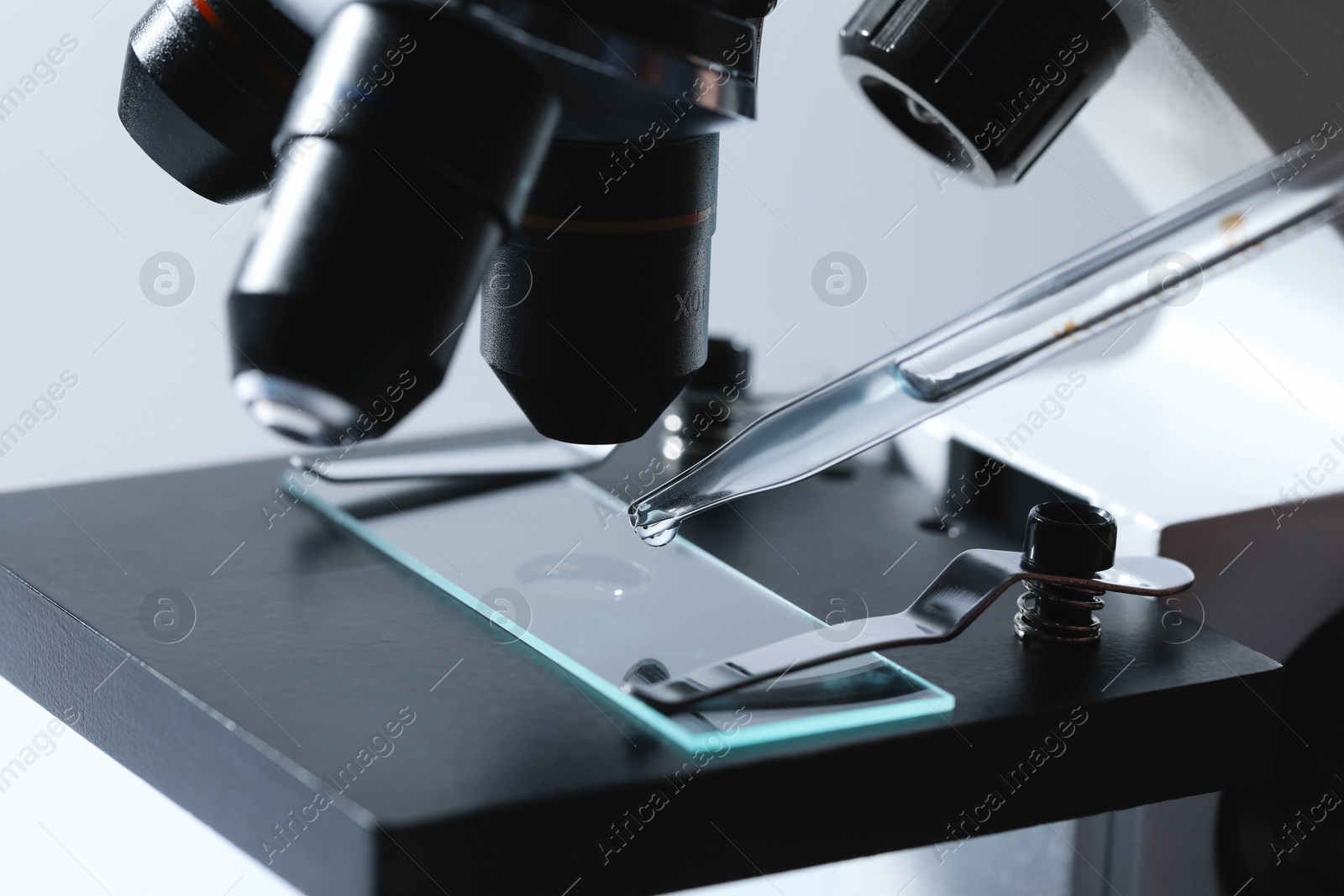 Photo of Dripping liquid from pipette onto glass slide on microscope, closeup