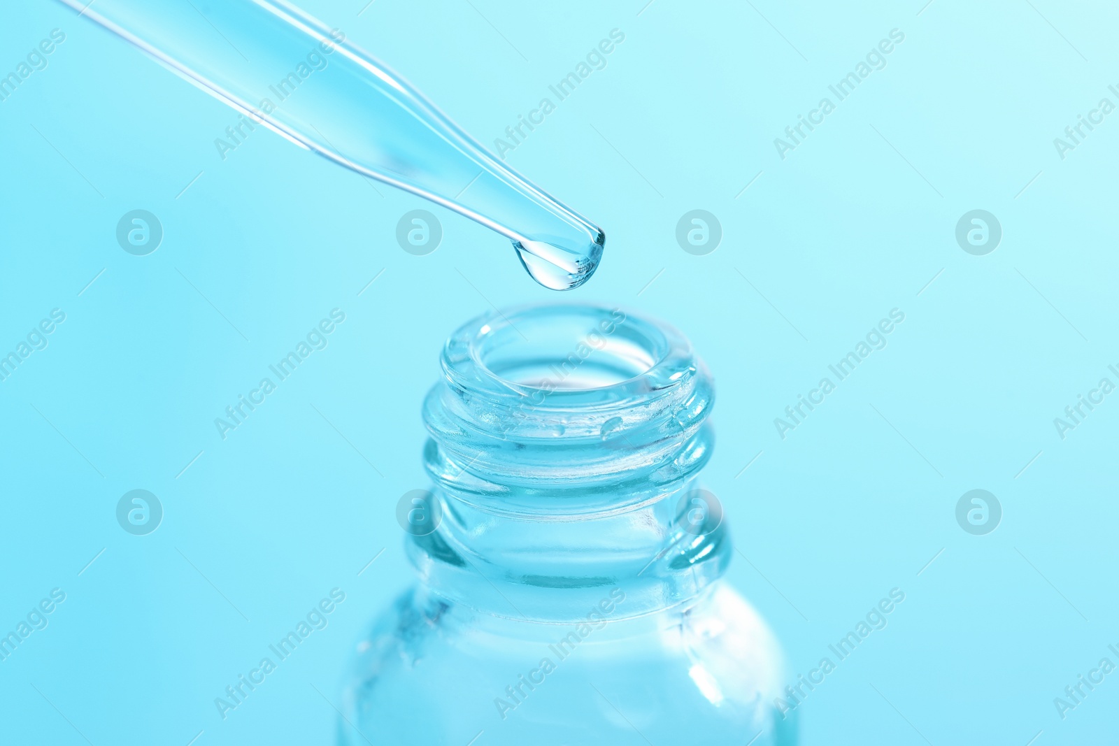 Photo of Dripping liquid from pipette into glass bottle on light blue background, closeup