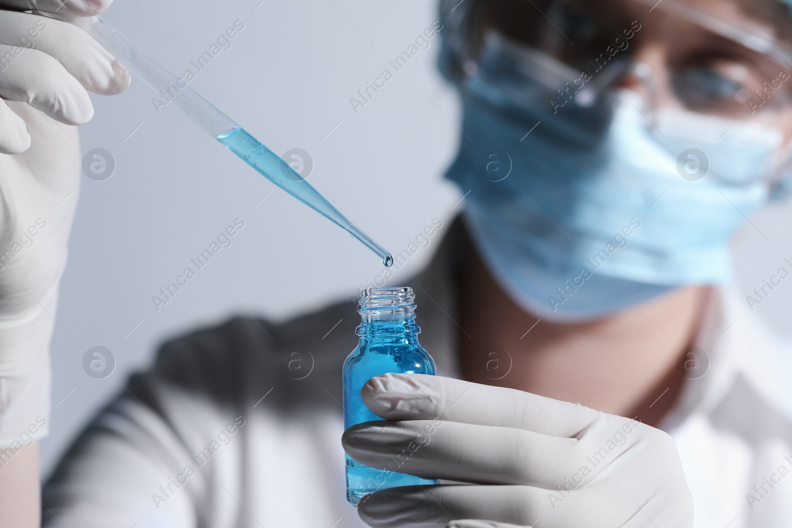 Photo of Scientist dripping liquid from pipette into glass bottle on light background, closeup