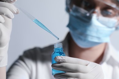 Scientist dripping liquid from pipette into glass bottle on light background, closeup